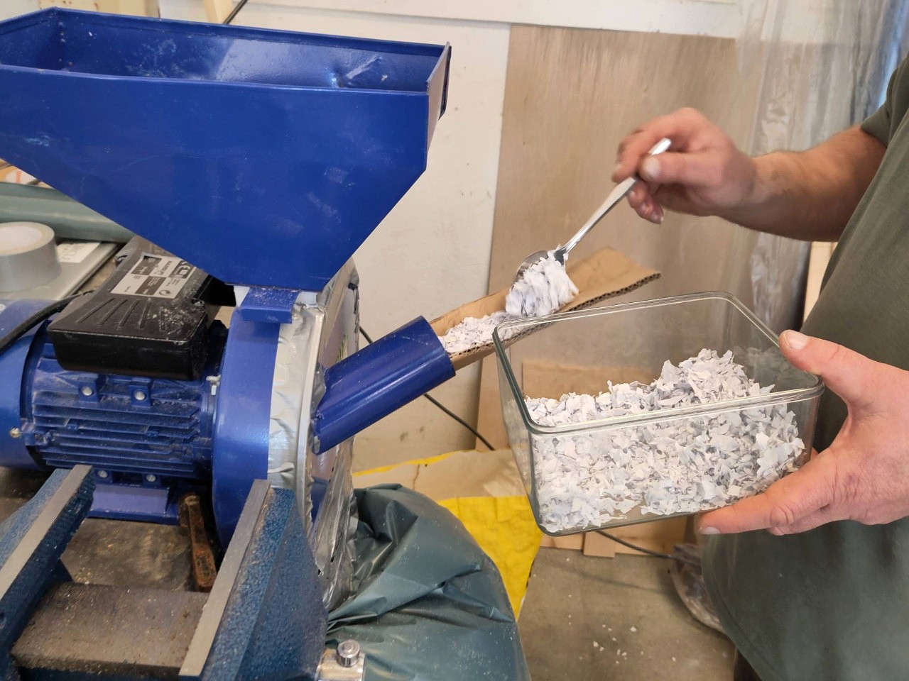 Hand met lepel voert papiersnippers in in blauwe machine